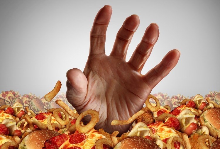 Obesity and overweight concept as the hand of a person emerging from a heap of unhealthy fast food and desperately reaching out for diet and dieting help as a symbol of bad nutrition proplems.